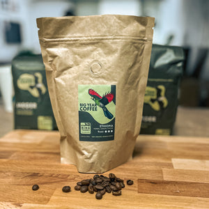 8oz bag of ethiopian natural grade one sits on a wood cutting board with coffee beans displayed in front